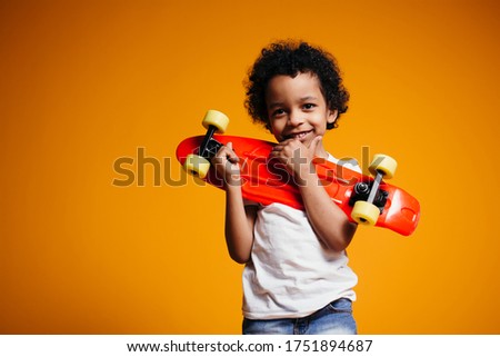African American Boy in white T-shirt and jeans hugs a red skateboard and presses it to his chest