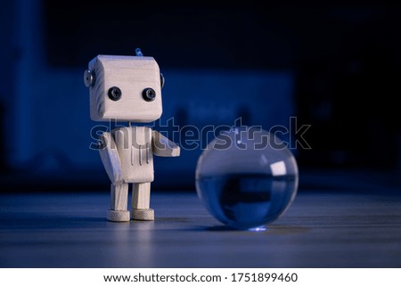 A small wooden toy robot looks at a glass ball in the dark. wallpaper, blured background. low light. eco friendly toy