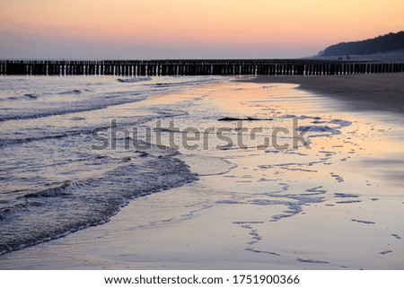 Beautiful sunset colors on the beach of sea and amazing reflection in water. Silhouette of breakwater on horizon.