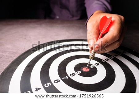 Closeup hand of businessman take a red dart hit on the center of dartboard, goal setting, target your customer, or marketing plan concept Royalty-Free Stock Photo #1751926565