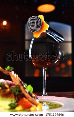 The microphone is lying on a glass of wine. The concept of a karaoke restaurant.Photo on a dark background in the room. Copy space.