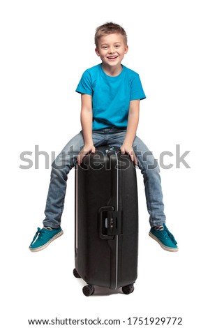HAPPY LITTLE BOY SITTING ON HIS PACKED SUITCASE ISOLATED ON WHITE BACKGROUND, TRAVELLING CONCEPT