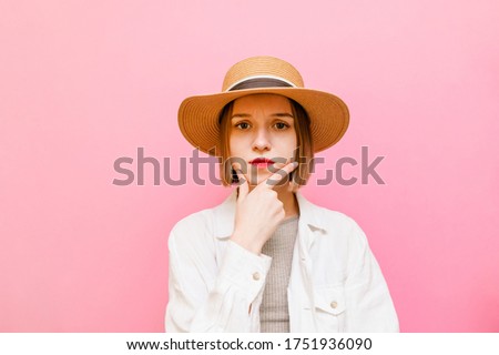 Pensive sad girl in light clothing and hat isolated on pastel pink background, looking into the camera at copy space and thinking. Pretty lady going through a pink background.