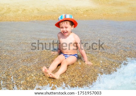 a happy boy is sitting in the water on the beach and splashing in the waves. A child enjoys the sea