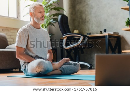 Middle aged sport man doing yoga and fitness at home using laptop Royalty-Free Stock Photo #1751957816