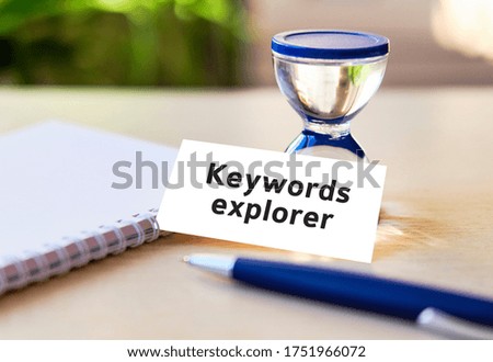 Keyword rank - business seo concept text on a white notebook and hourglass clock, blue pen, green leaves of flowers