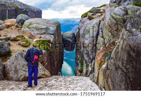 Tourist man takes a photo of the most dangerous stone in the world of Kjeragbolten. Kjeragbolten is a rock stuck at an altitude of 984 meters above Lysefjorden on mountain Kjerag, Norway.