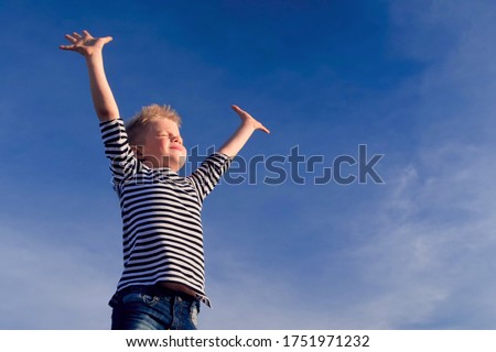 Relaxed boy breathing fresh air raising arms over blue sky at summer. Dreaming, freedom and traveling concept. Royalty-Free Stock Photo #1751971232