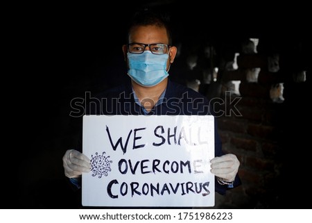 A young man wearing a medical mask and safety gloves stands with a placard message to "We shall overcome Coronavirus". A man holding a placard Massage.