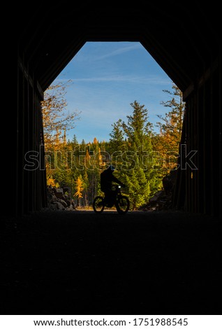 Mysterious man on dirt bike captured in silhouette frame with contrasting autumn landscape with vibrant colors