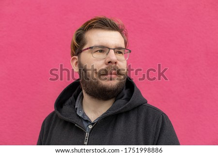 urban photography of good mood middle adult person in glasses with beard looking side ways, bright colorful pink wall background texture space 