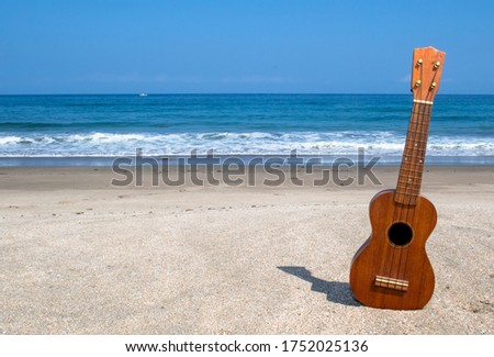 Ukulele on the sand at a beach with a blue ocean in the background, also with various objects
