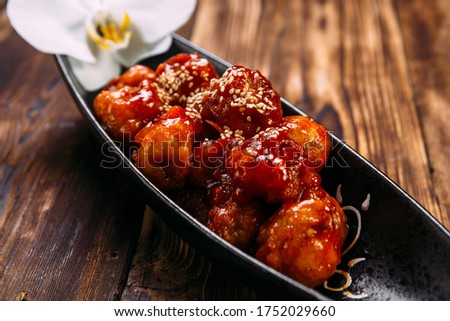 Closeup on asian batter chicken with spicy sweet sauce on the black plate on the wooden table, horizontal