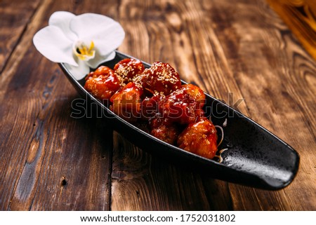 Asian batter chicken with spicy sweet sauce on the black plate on the wooden table, horizontal