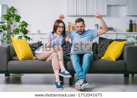 Young excited overjoyed couple of football fans looking at their laptop computer screen with astonished face expression celebrating favourite team touchdown and winning money at bookmaker's website. Royalty-Free Stock Photo #1752041675