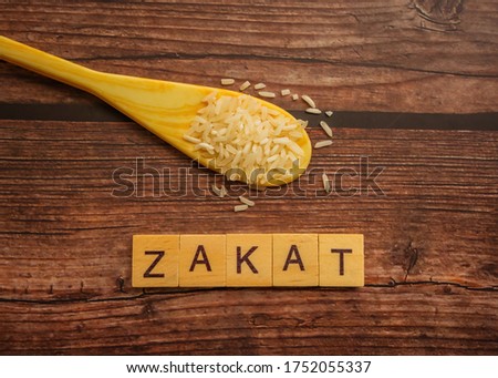 Conceptual zakat (islamic tax) with rice. Obligation to aid the poors. ZAKAT text on wooden table. Islamic zakat concept. Selective focus.