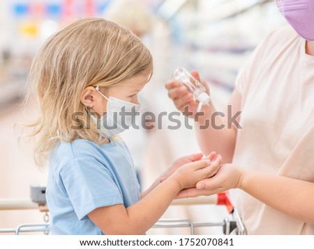 Mother applies sanitizer for cleaning baby's hands in a shop during coronavirus and flu outbreak.