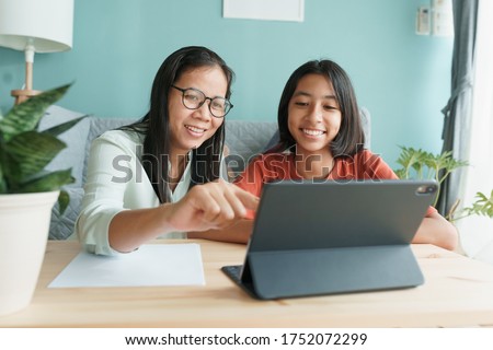 Asian family with a daughter do homework by using tablet with mother help. Happy smile Asia kid while sitting in the living room at home morning. Concept of online learning at home Royalty-Free Stock Photo #1752072299
