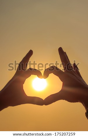 Silhouette image of hands making a heart or love shape with the sun in the center. 
