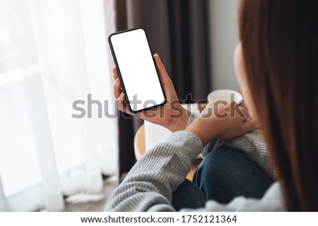 Top view mockup image of a woman holding mobile phone with blank desktop screen while sitting in bed room at home