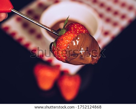 Chocolate fondue kit and fresh strawberry coveren with chocolate, black background.