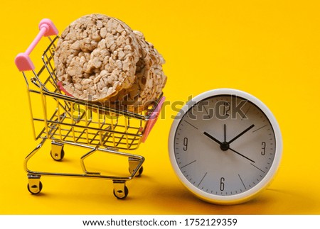 Diet concept. Shopping trolley with whole grain crispbreads and clock on yellow background 