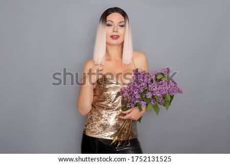 Young stylish blonde woman dressed in a golden top holds in her hands a large bouquet of lilacs. studio shot