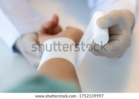 Close up photo with selective focus.Asian orthopaedic doctor using the white elastic bandage roll over the patient 's wrist. Wrist pain from sport injury. Shallow DOF.Medical concept.