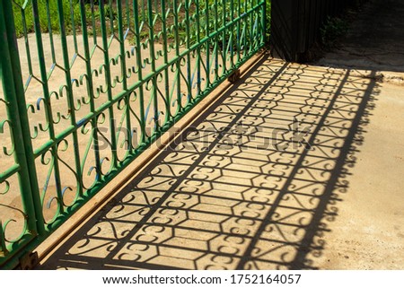 Shadows of the iron gate with parallel bars visible on the concrete ground.