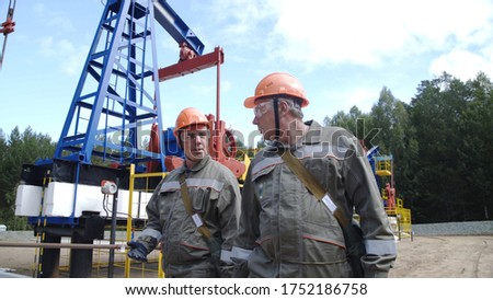 Two male oil workers walking and talking near oil pump jacks. Engineers overseeing drilling rig of crude oil production. Pumping crude oil for fossil fuel energy with drilling rig in oilfield.