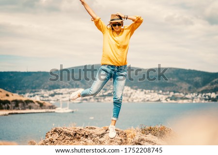 Happy young woman in a yellow shirt and hat rejoices on the seashore with a view, summer vacation and travel. Image with retro toning.