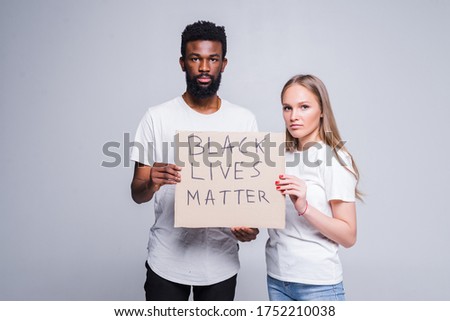 Young african man and caucasian woman holding a cardboard poster with the message text BLACK LIVES MATTER isolated on white background.