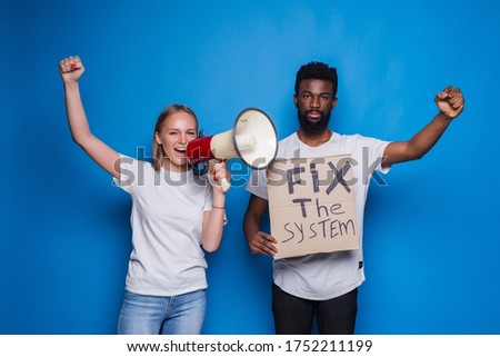 Young caucasian woman with megaphone and African man holding a cardboard poster with the message text FIX THE SYSTEM on blue background. 