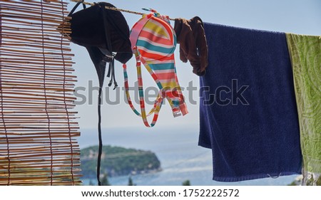 Colorful striped bikini hanging out to dry on a washing line next to beach towels in summer on a greek island by the mediterranean sea.