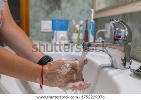 side view of a woman's hands while washing under a tap with soap