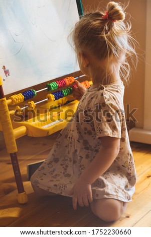 Little girl sits on the floor and draws on an easel