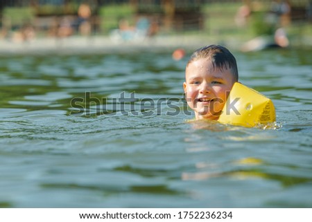 little toddler kid swimming in lake with inflatable arms aids support