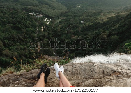 Couple of  travel bloggers explore beautiful places in Sri Lanka island.  Pictures of legs travel coupl wearing sneakers sit on the top of waterfall