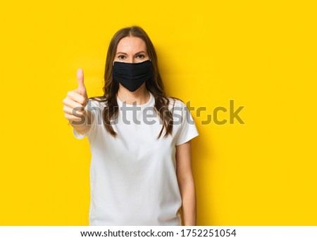 Young adult woman portrait with finger up in medicine mask on yellow background, pandemic concept, copy space