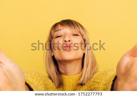 Young beautiful woman isolated over yellow background. holding camera with hands and talking selfi or self-portrait. Girl wear yellow sweater