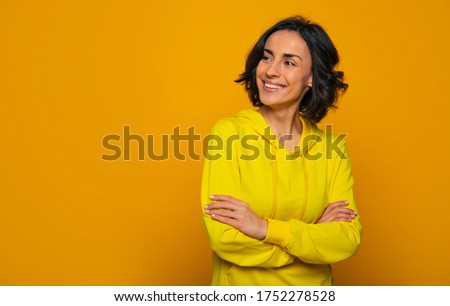 Happy sight. Half-length photo of a toothy smiling girl with her hands crossed on chest, looking positively radiant, dressed in a yellow hoodie, looking sideways. Royalty-Free Stock Photo #1752278528