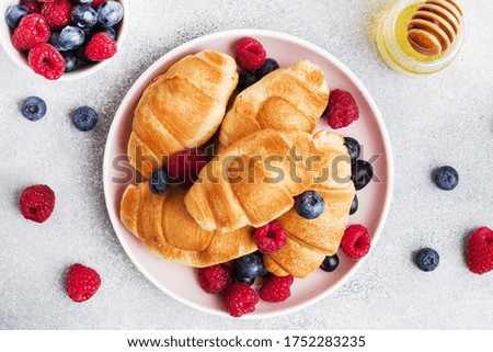 Croissants with fresh raspberries and blueberries on grey concrete background. Copy space. concept of Breakfast coffee honey