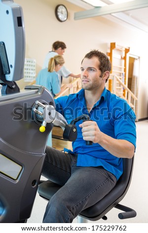Young man on exercise bike with physical therapist assisting patient in hospital