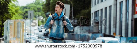 Panoramic shot of handsome delivery man with thermo backpack on urban street