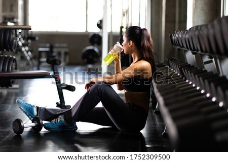 Female athlete taking rest and drinking woter after exercising at gym. Fitness Healthy lifestye and workout at gym concept.