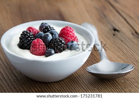Bowl of fresh mixed berries and yogurt with farm fresh strawberries, blackberries and blueberries served on a wooden table Royalty-Free Stock Photo #175231781