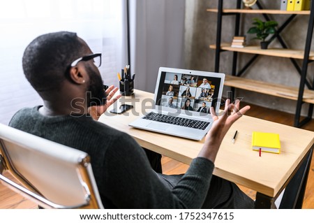 Virtual meeting with many people together. African-American young guy talking online with employees via video connection. Multiracial team. Back view Royalty-Free Stock Photo #1752347615