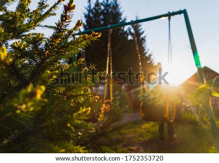 A teenage boy in a green jacket is thoughtful. A child swings on a swing. Beautiful sunlight. Sunset.