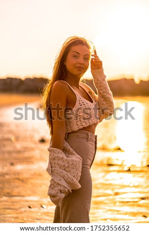 Summer lifestyle, a young blonde with straight hair, wearing a small wool sweater and corduroy pants on the beach. Enjoying the sun at sunset looking at camera, vertical photo