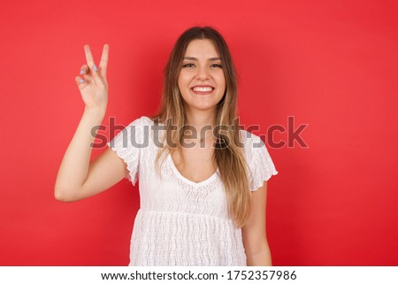 Young caucasian woman standing against gray wall showing and pointing up with fingers number two while smiling confident and happy.